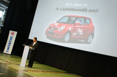 Baki a prezentációban - Takeuchi Hisashi mögött egy előző generációs Swift-et mutatnak a jubileumi matricázással